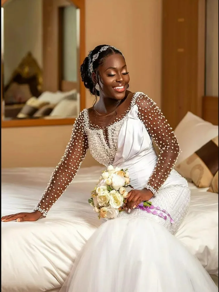 ชุดแต่งงานแบบแอฟริกันสั่งตัดพิเศษ คอเสื้อโปร่งประดับมุกเงางาม พร้อมชายกระโปรงยาวแบบสปีว์เทรน แขนยาวคลาสสิก หรูหรา