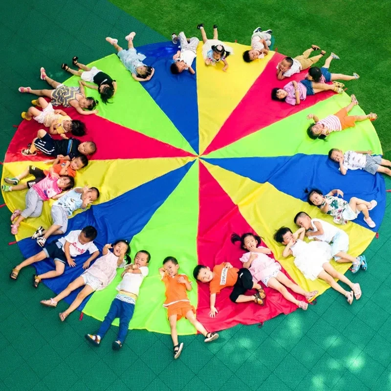 Várias pessoas acampamento ao ar livre arco-íris guarda-chuva pára-quedas brinquedo salto-saco ballute jogar interativo jogo de trabalho em equipe