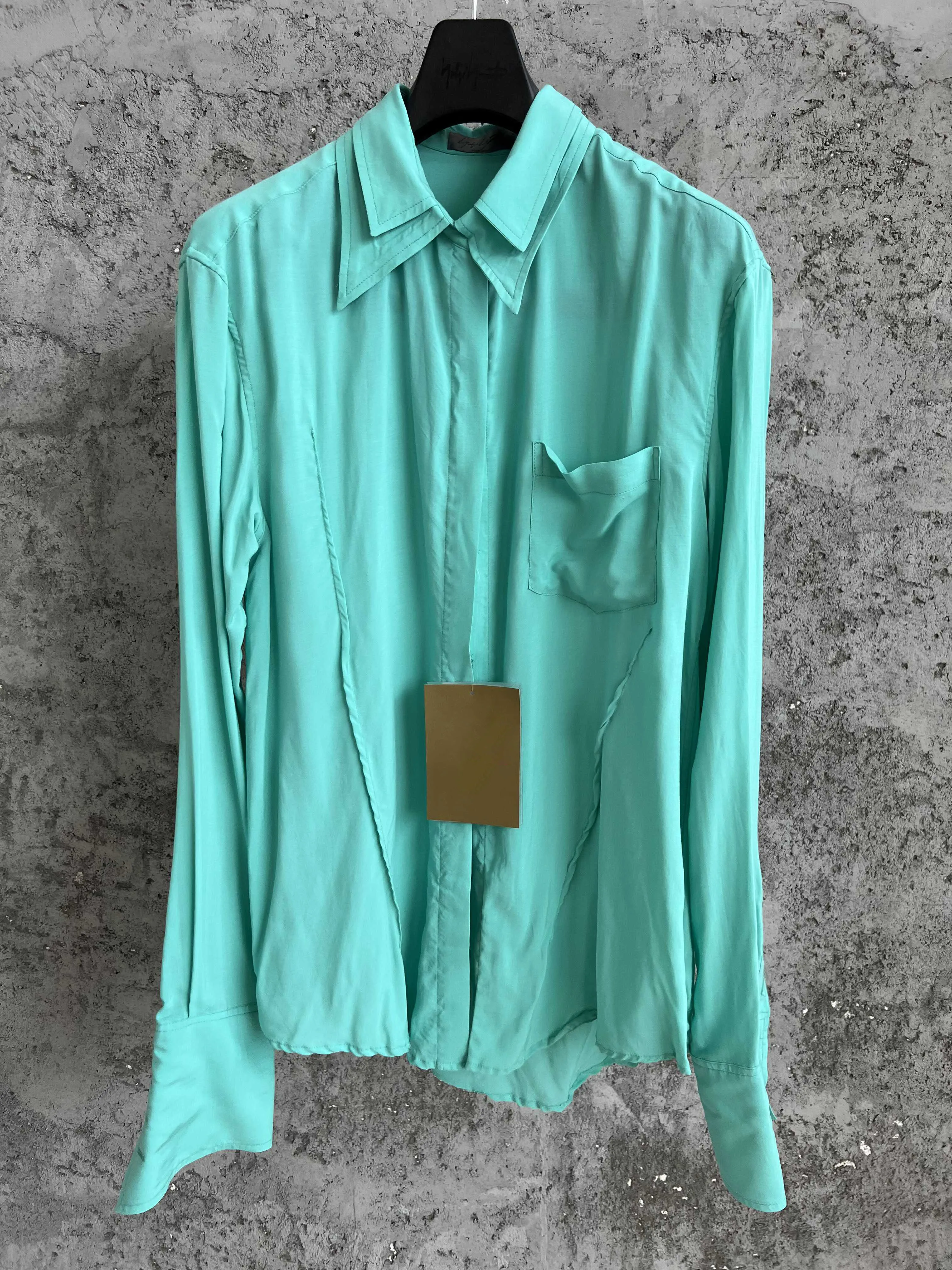 A short front and long back side-slit shirt made of pure cotton with a pointed collar, long sleeves, and a single-breasted openi