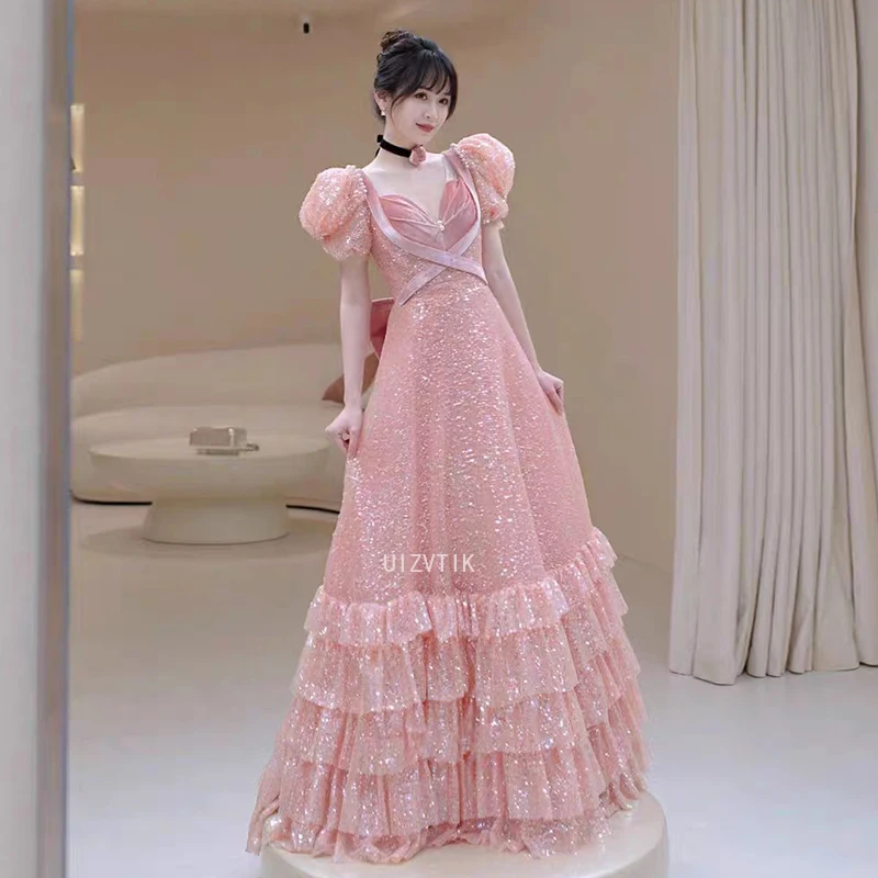 ชุดราตรีสีชมพู แขนพองสั้น คอวี ประดับเลื่อม แต่งโบว์ พร้อมระบายชายกระโปรงยาวลากพื้น สำหรับงานพรอมหรืองานเลี้ยงอย่างเป็นทางการ