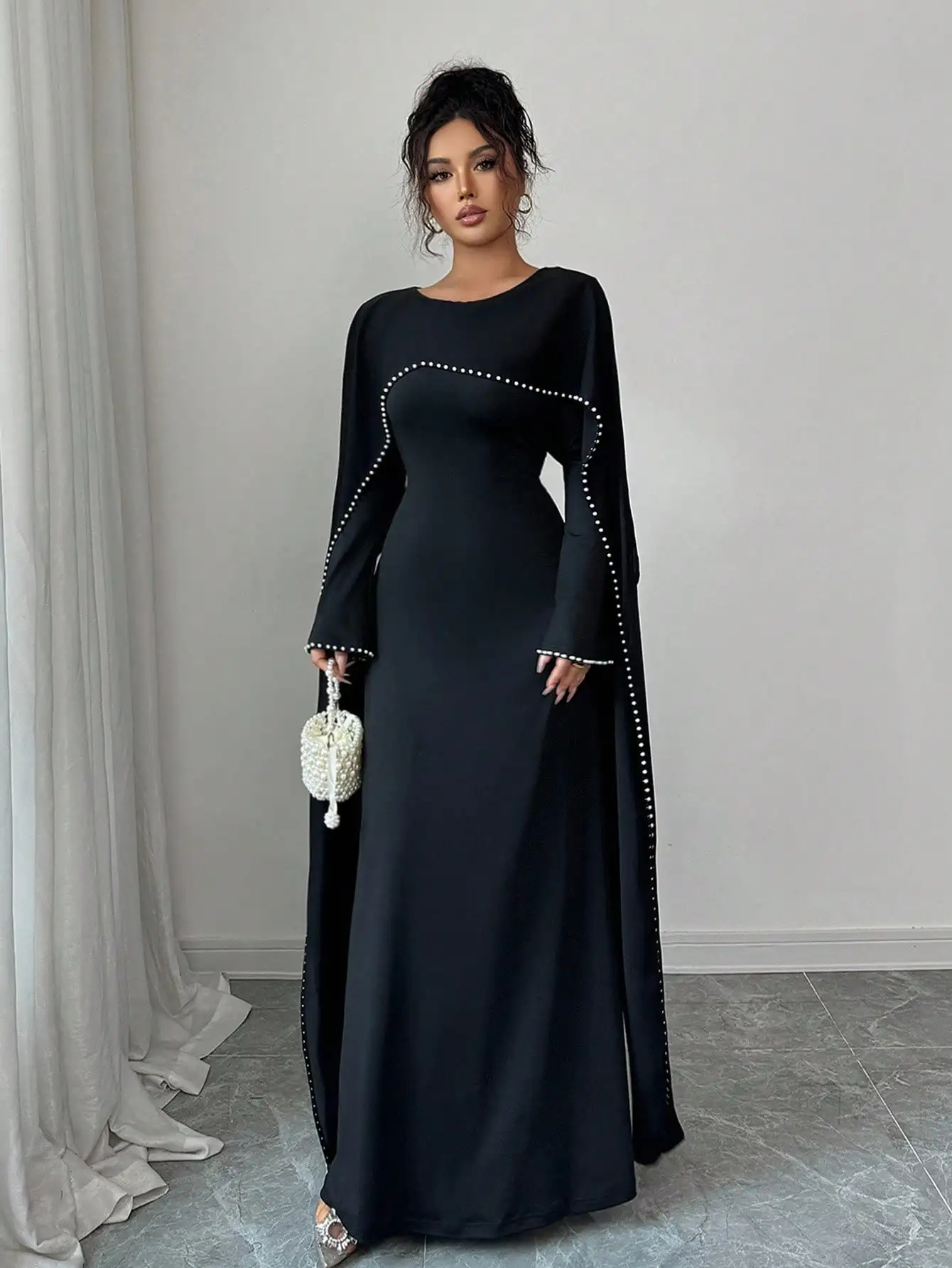 

Элегантное черное длинное платье с рукавами-накидками, украшенными жемчугом, и круглым вырезом горловины.