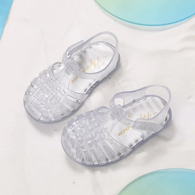 

Сандалии для маленьких девочек, новинка лета 2024, радужные детские римские пляжные сандалии, защищающие от столкновений, детские прозрачные сандалии с кристаллами