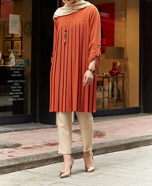 Angled front view of rust pleated tunic showing its longline hem and sleeve tabs