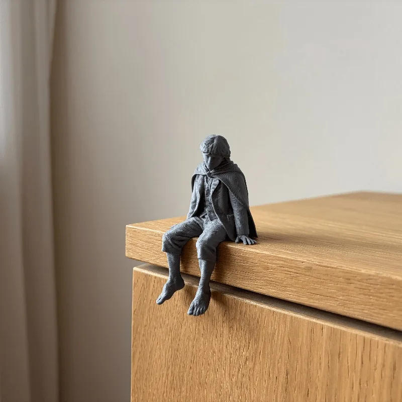1/3 Piece Set of a Humble Traveler Figurine for Display on the Edge of a Shelf or Desk, Featuring a Classic Cape and Barefoot Design, with Legs Hanging from the Shelf, Making It the Perfect Companion Statue for a Home