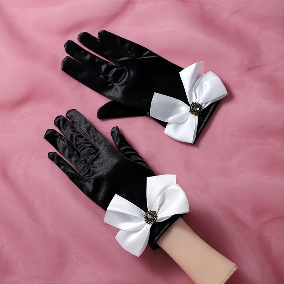 A pair of black wrist length gloves with bow decorations suitable as accessories for bride weddings or women's dances