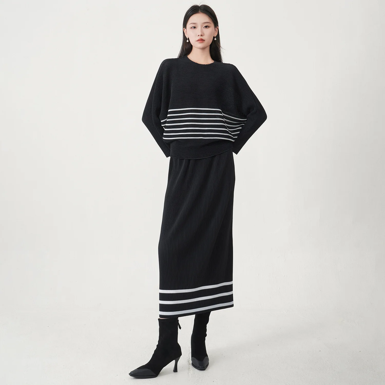 

A trending women's clothing item for 2026: a matching black batwing-sleeved striped T-shirt and straight-cut skirt set by Miyake