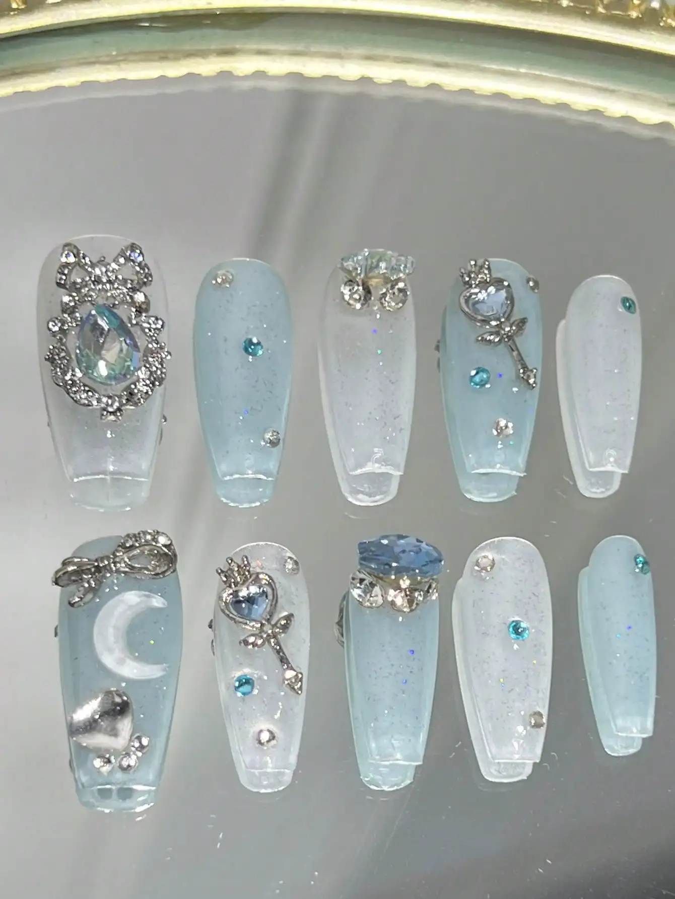 

10-Piece Long Coffin-Shaped Nail Art Set In A Blue, Intense-Glitter "Pure And Charming" Style. The Full-Coverage Press-On False Nails Are Adorned With Rhinestone-Encrusted Bows, Flower Wreaths, Moon-Shaped Rhinestones, Wands, Heart Rhinestones, And Blue "
