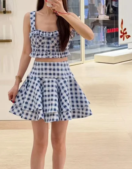 

Комплект: сине-белый жилет без рукавов с квадратным воротником и принтом в клетку, а также мини-юбка с рюшами