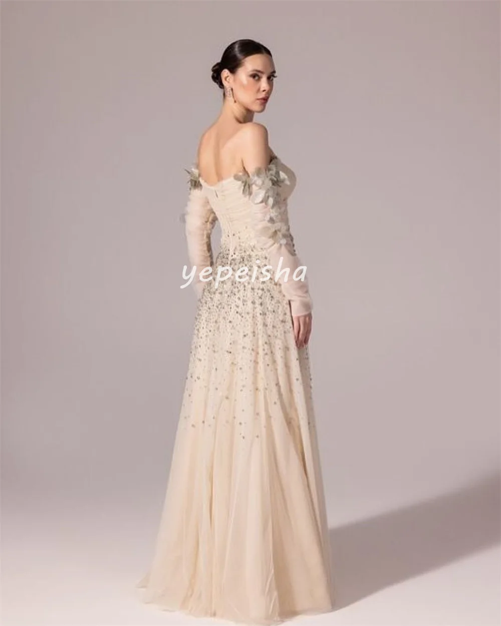 ชุดราตรีทรงเอไลน์แบบเปิดไหล่ ประดับด้วยผ้าทูลล์ระยิบระยับ แต่งดอกไม้ ลูกปัด และเลื่อม ดีไซน์หรูหรา