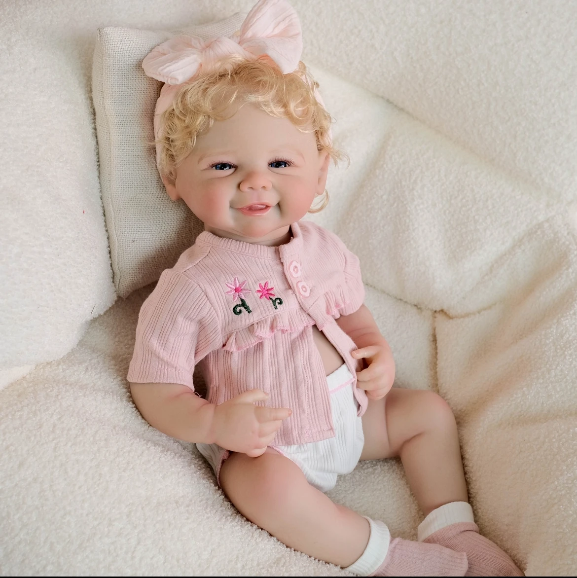 Boneca reborn de 48 cm com cabelo dourado implantado à mão, usando macacão de renda rosa e faixa de cabeça com laço, presente colecionável feito à mão