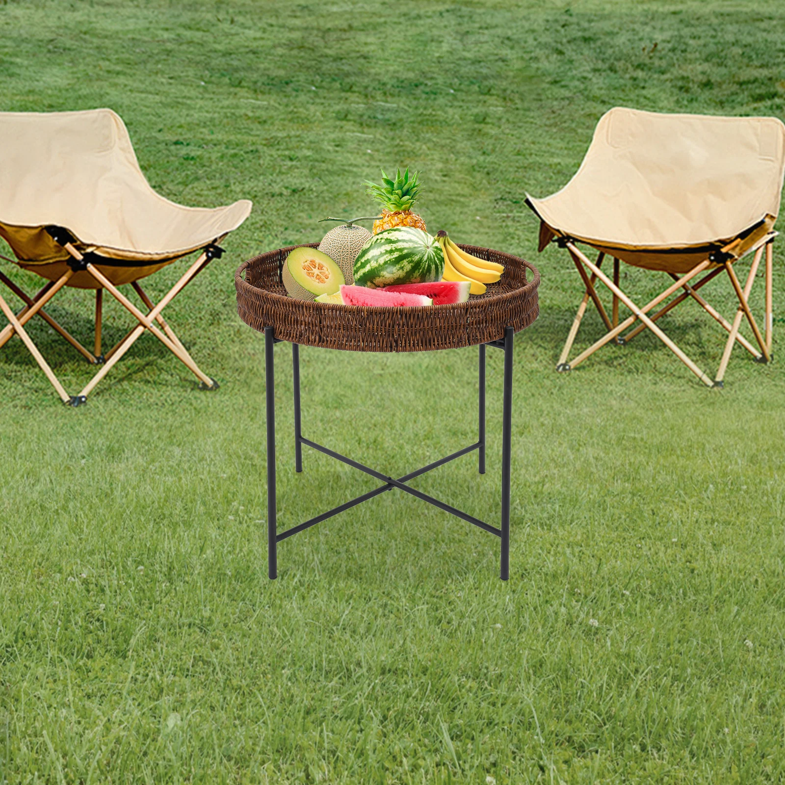 Rotan bijzettafel in het gras tussen twee camping-klapstoelen met fruit en meloen als borrelplank