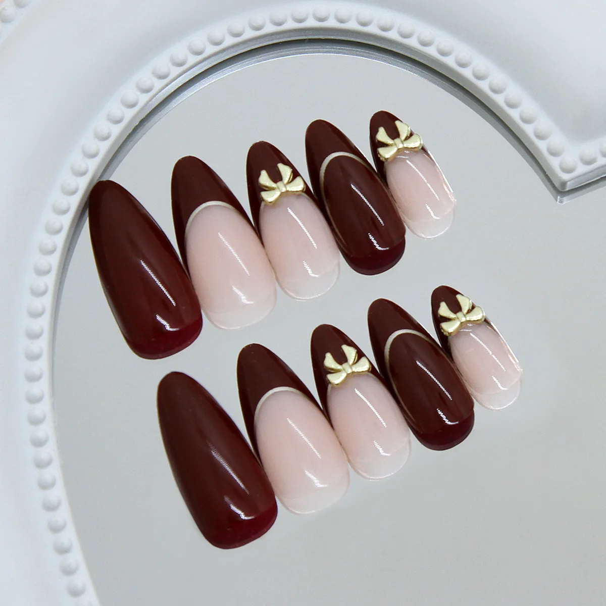 24 handmade almond nails. Burgundy base with nude French, white lines & metal bows. Reusable, elegant retro style for daily wear
