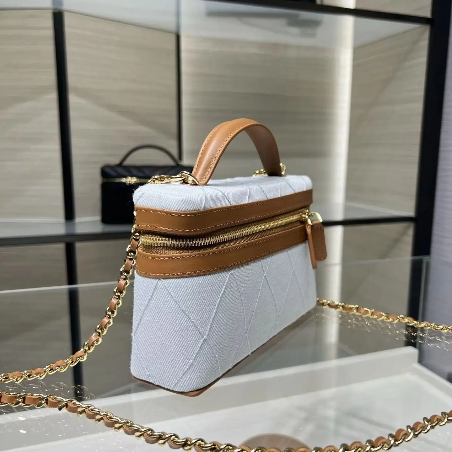 Light blue quilted fabric handbag with tan leather trim, short top handles, and a rectangular crossbody shape with a leather-woven gold chain strap.