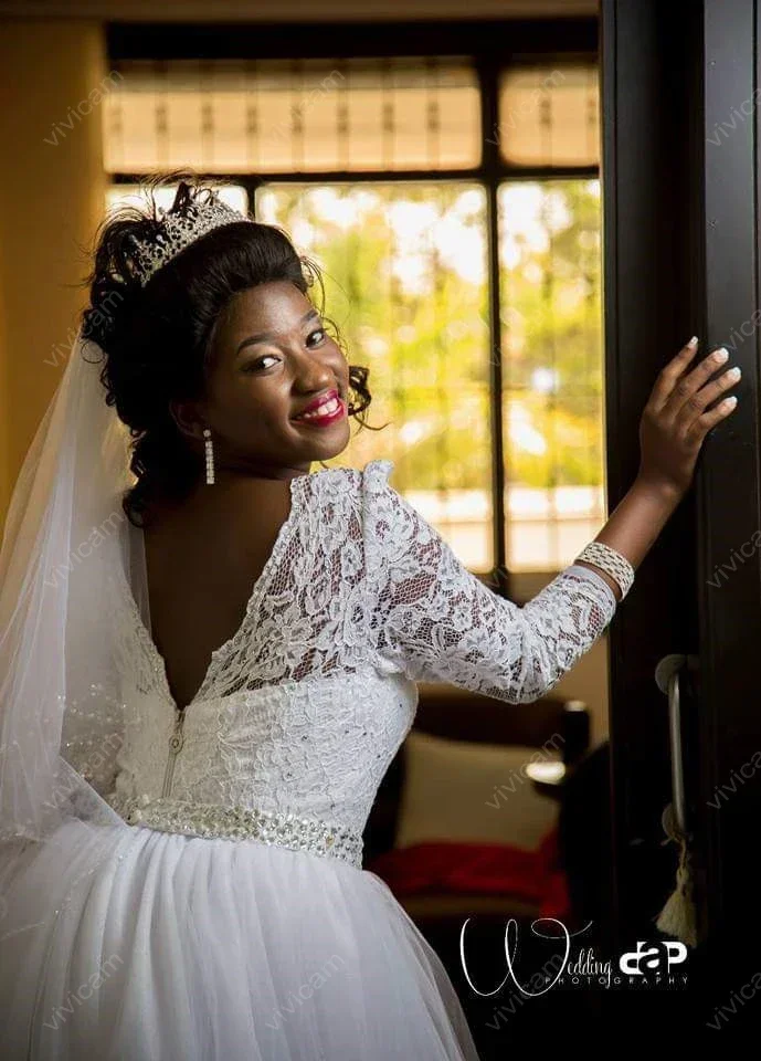 Suknie ślubne z koronką, dekoltem w łódkę, długimi rękawami, odpinanym trenem i odkrytymi plecami, zdobione uroczy, personalizowane kryształki.