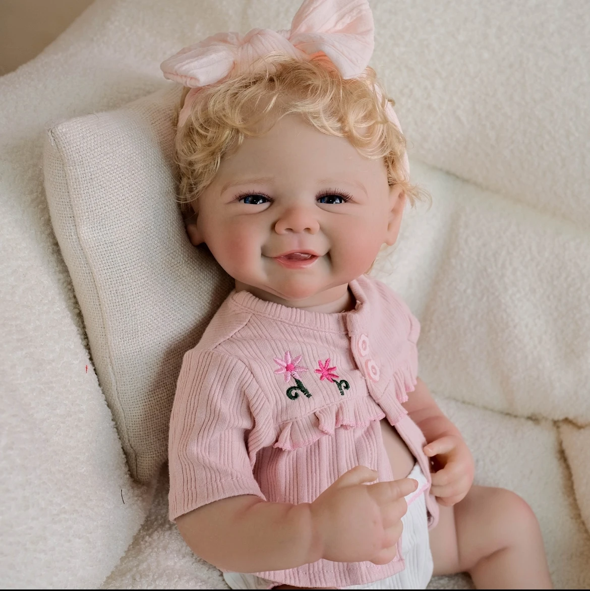 Boneca reborn de 48 cm com cabelo dourado implantado à mão, usando macacão de renda rosa e faixa de cabeça com laço, presente colecionável feito à mão