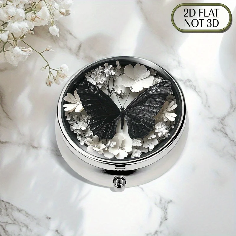 A flat, portable, round metal pill box, featuring a black butterfly and white floral design, offers three compartments for organized medication storage, ideal for storing vitamins, small accessories, and coins, a perfect gift.
