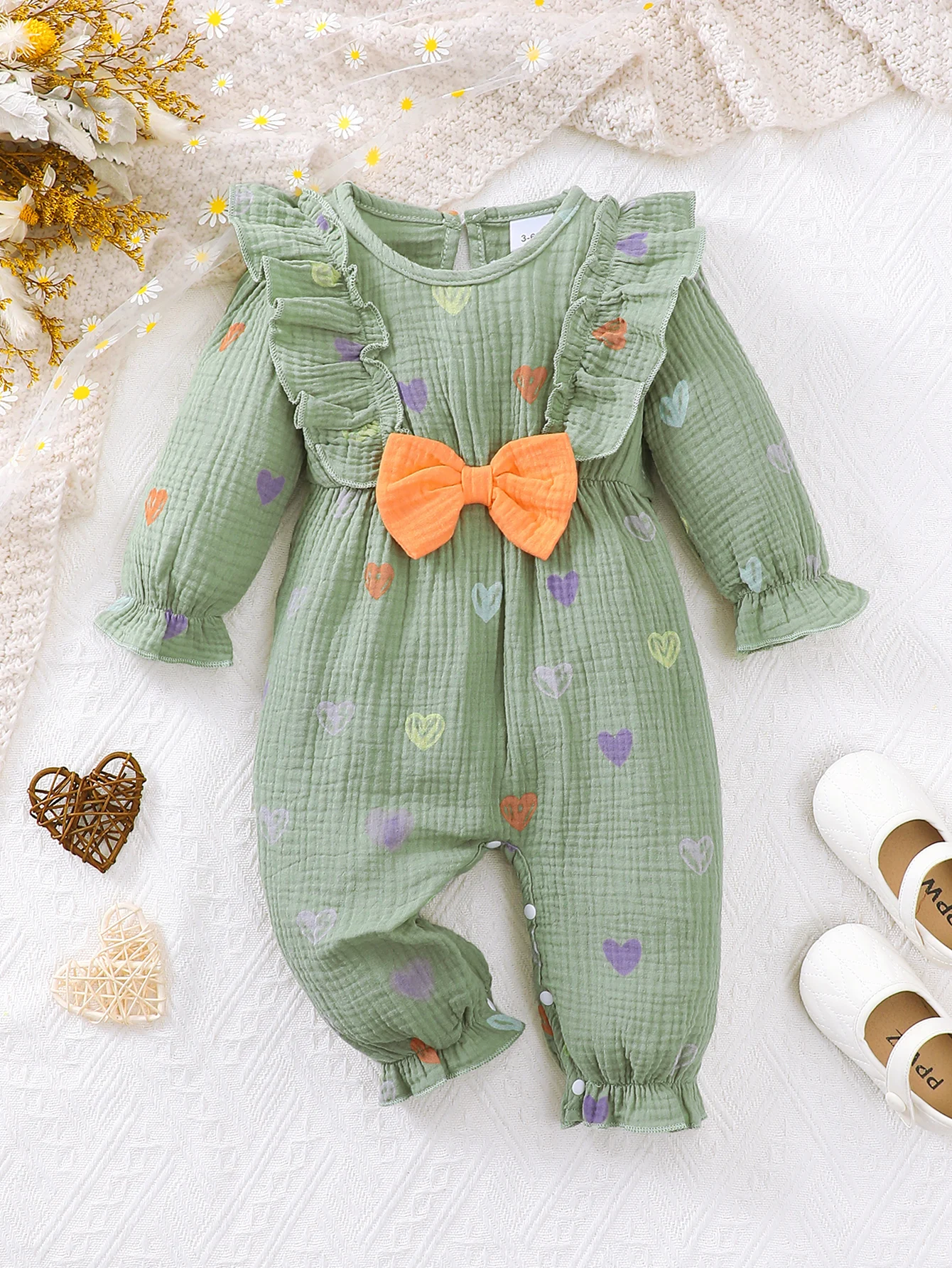 Baby Girl's Spring and Autumn Long-Sleeved Romper, in a Fresh Green Color, with Colorful Heart Patterns Printed All Over, Delicate Ruffled Edges on the Shoulders, and a Striking Orange Bow on the Chest, with Hidden Snaps at the Bottom for Easy Diaper Changes, Suitable for Daily Wear, Outings, and Photoshoots, a Sweet and Cute Infant Jumpsuit.