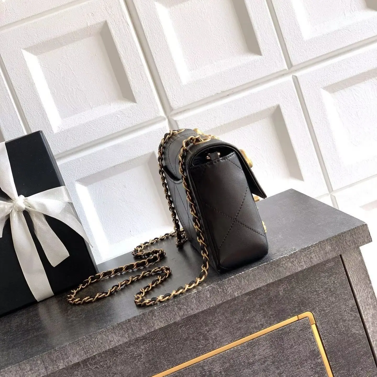 Black diamond-quilted leather flap crossbody bag, decorated with small metal charms (flowers, hearts, bows, and pearls), with a detachable gold chain shoulder strap.