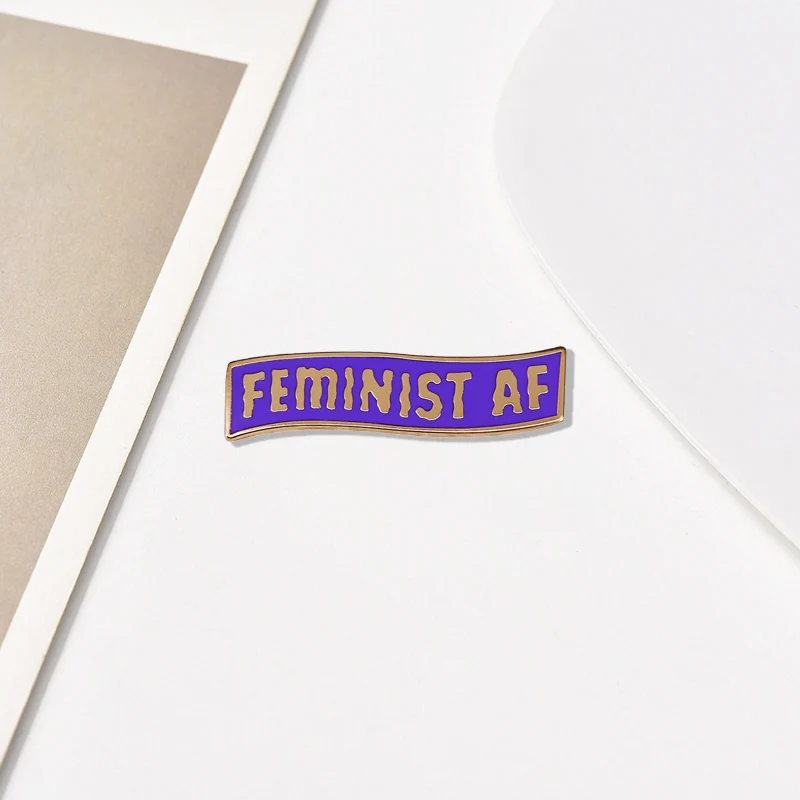 Feminist AF brooch with a purple background and golden letter logo badge