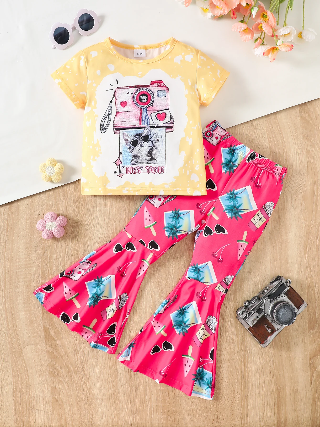 A two-piece summer set for girls consists of a T-shirt with cartoon cat prints and animated flared pants. Made of comfortable po