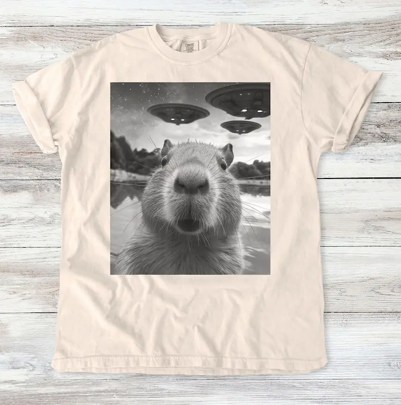 

Capybara vs. UFOs Meme T-Shirt - Hilarious Alien Encounter Graphic Tee - Scenic Lake Design