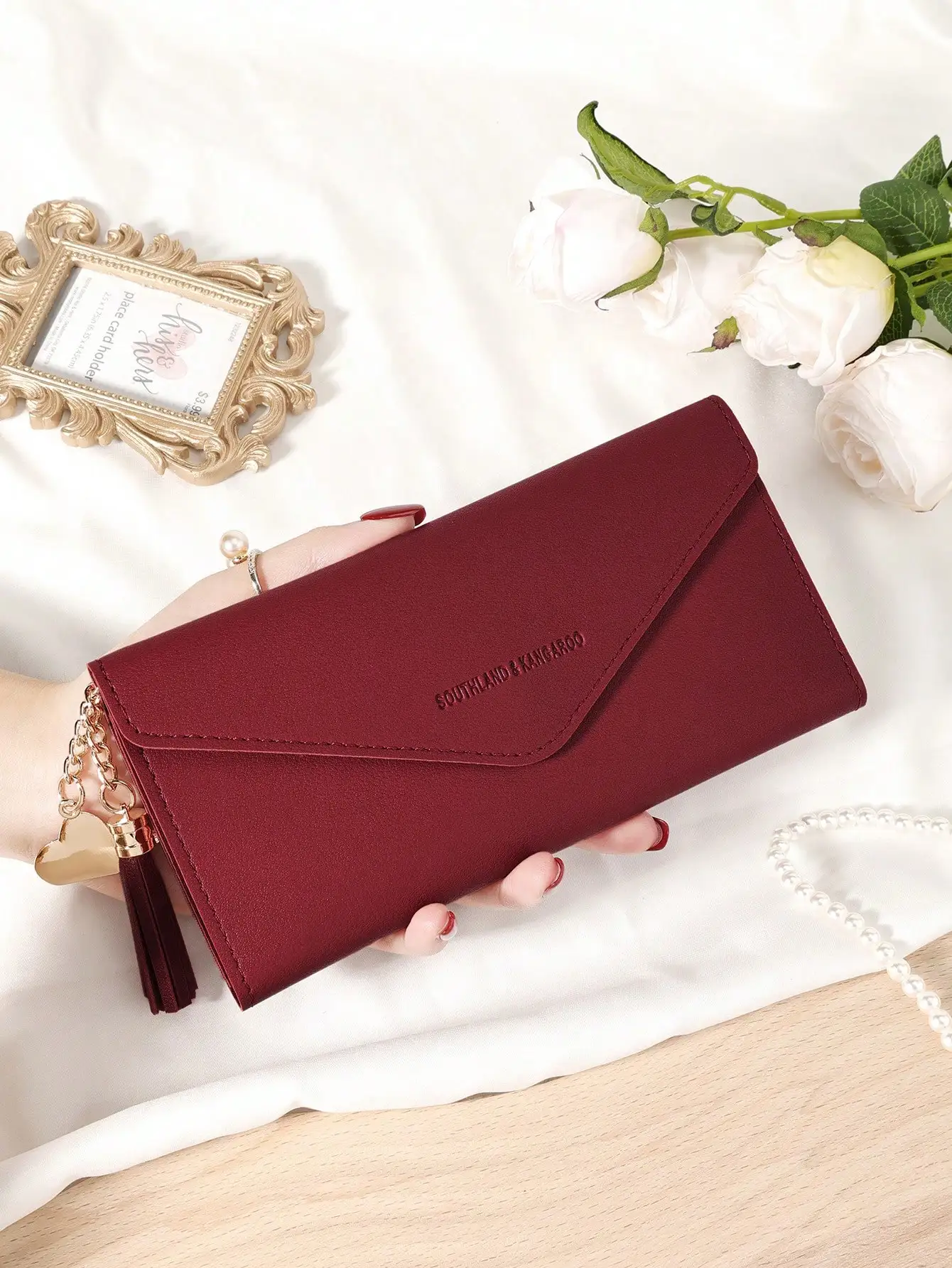 

Бордовый женский кошелек-трифолд с кисточкой и подвеской в виде сердца, множеством отделений для карт и карманом на молнии для монет