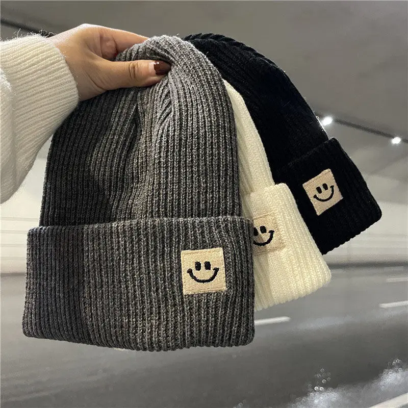 Gorro de punto negro con marca de cara sonriente japonesa para mujer, modelo de tendencia cálido de otoño e invierno, protector de oídos versátil, gorro de lana para hombre