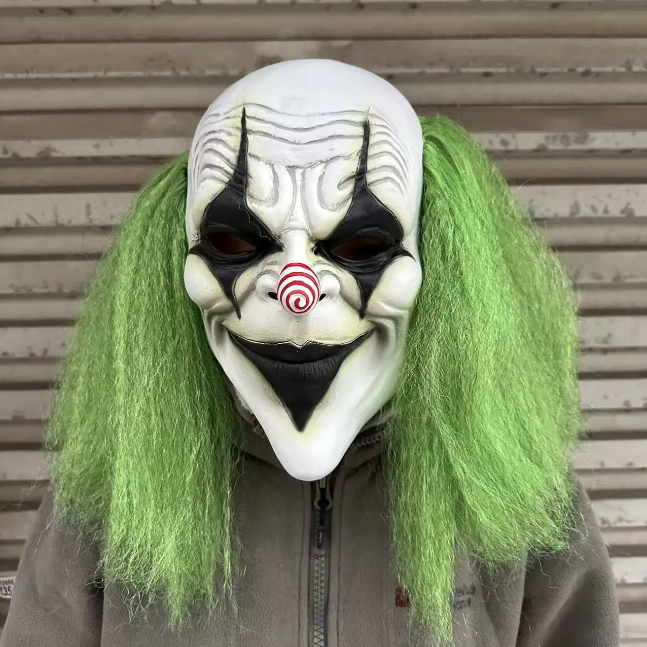 Furchteinflößender grünhaariger Clown mit Latexmaske und einer spiralförmigen rot-weißen Nase. Geeignet für Halloween-Kostümparty-Requisiten