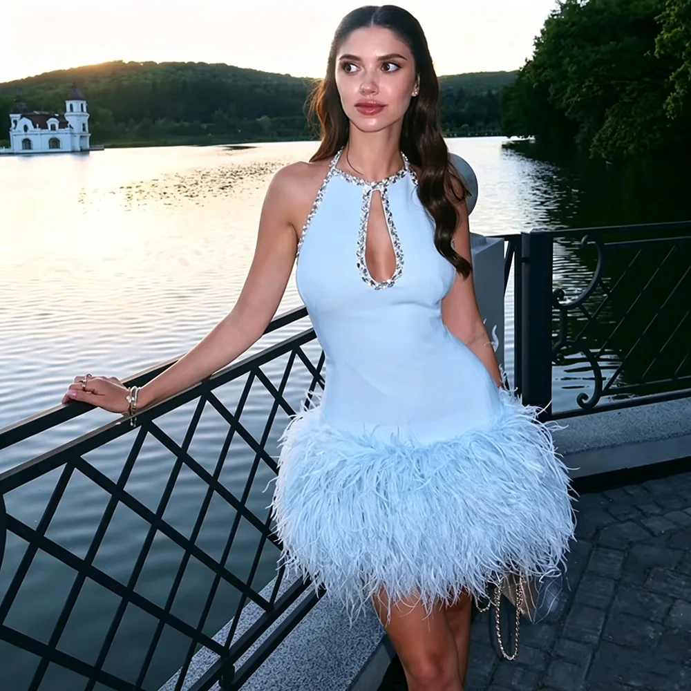 Impresionante vestido de noche de corte en A, de color azul celeste, con detalles de plumas y cristales, ideal para fiestas y eventos especiales. Vestido corto sin mangas, con escote halter, perfecto para cócteles y fiestas.