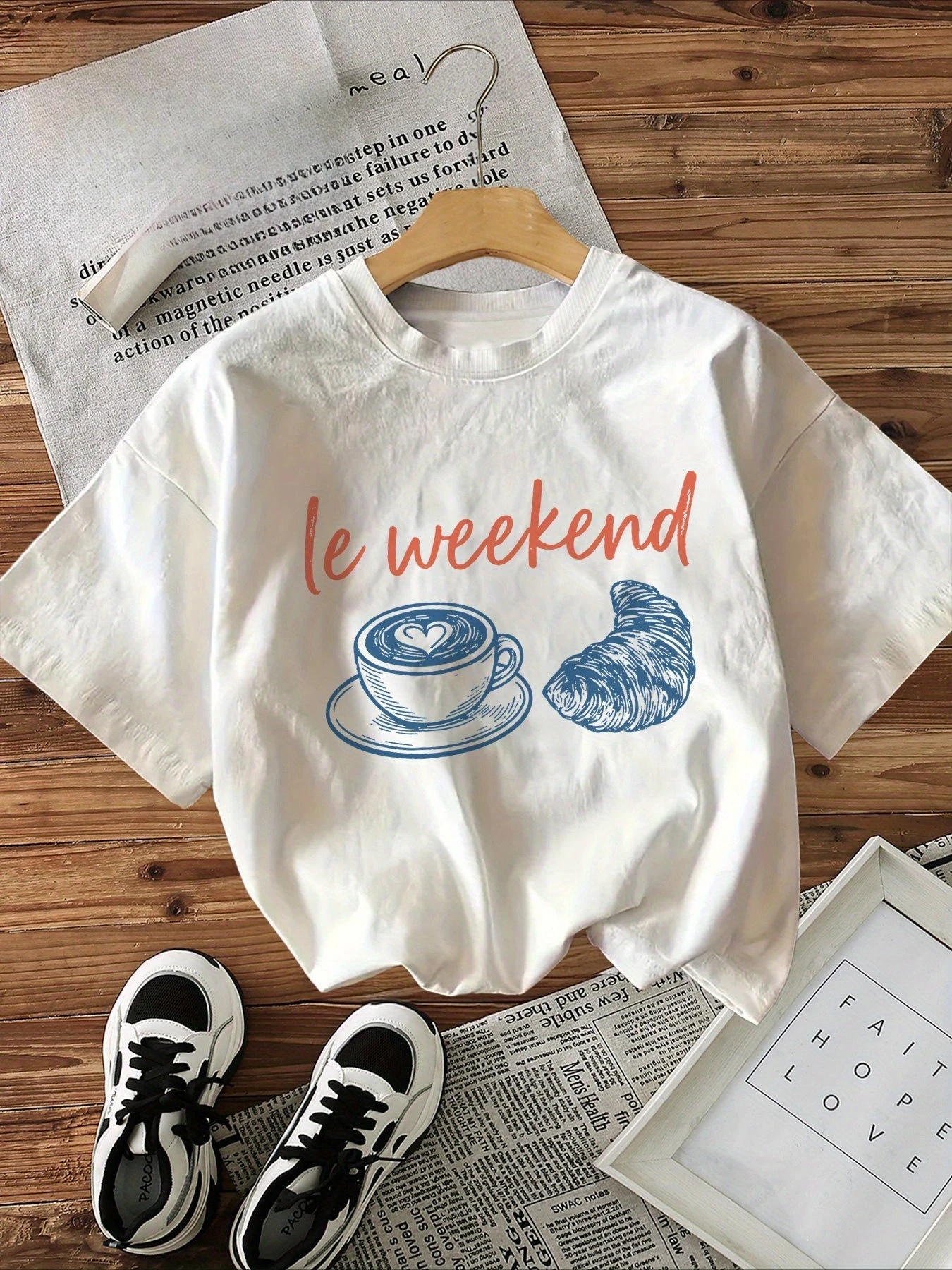 Camiseta gráfica de manga corta con cuello redondo para mujer, estilo casual, con estampado de café y croissant con letras naranjas.