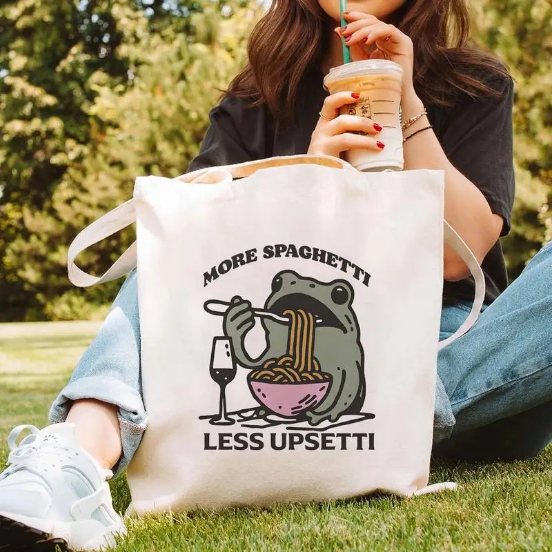 A tote bag with a cartoon pattern of a frog eating noodles，Lightweight and reusable canvas shoulder bag，Suitable for school、Trav