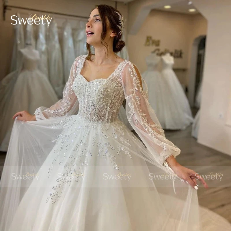 ชุดแต่งงานที่สง่างาม Organza เย็บปักถักร้อยประดับด้วยลูกปัด A-Line Ball Gown สแควร์คอแขนยาวชุดเจ้าสาวปุ่มที่กําหนดเอง