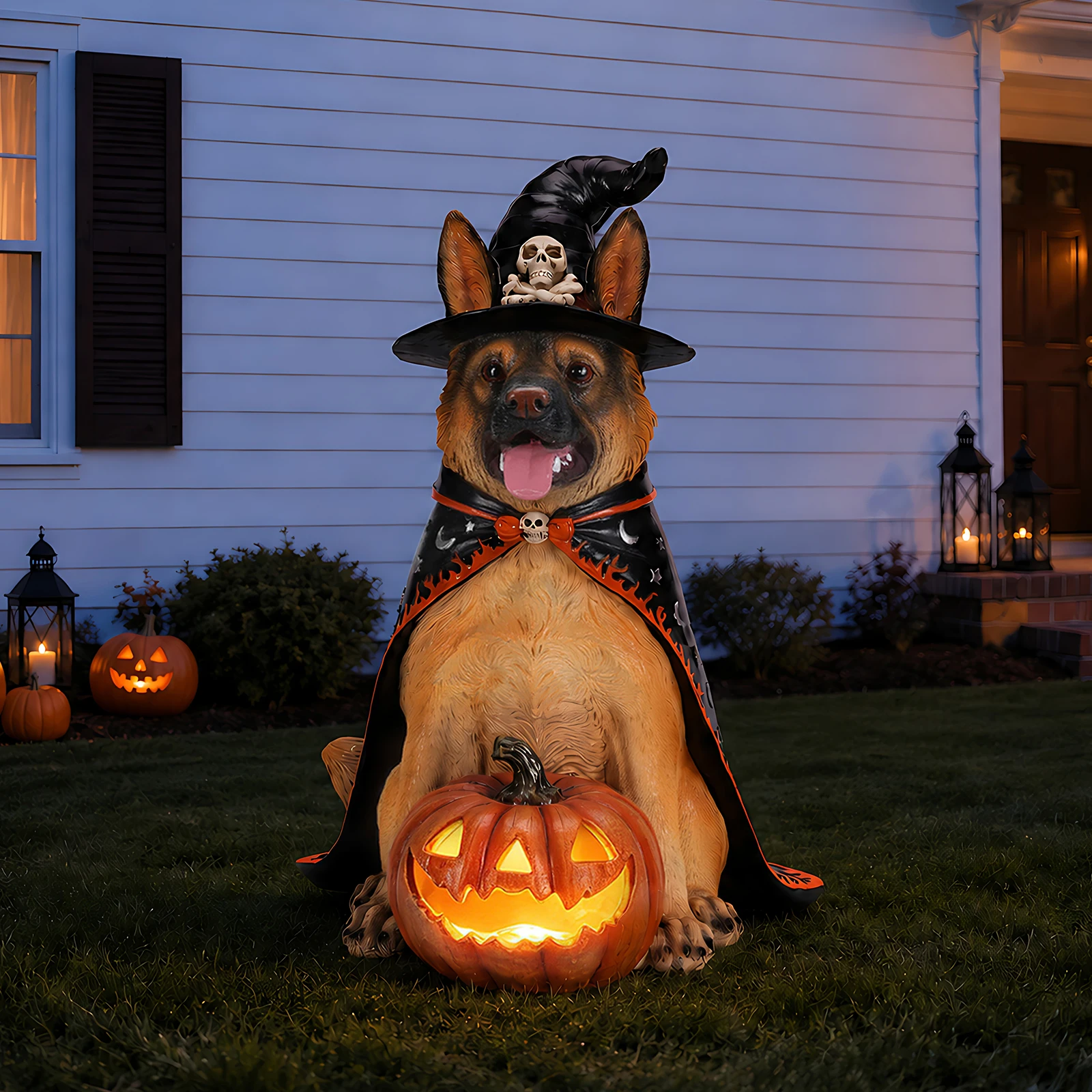 A weather-resistant resin Halloween statue of a sitting German Shepherd dog wearing a black witch hat and cape, holding a glowing orange LED jack-o'-lantern pumpkin on a lawn at night.