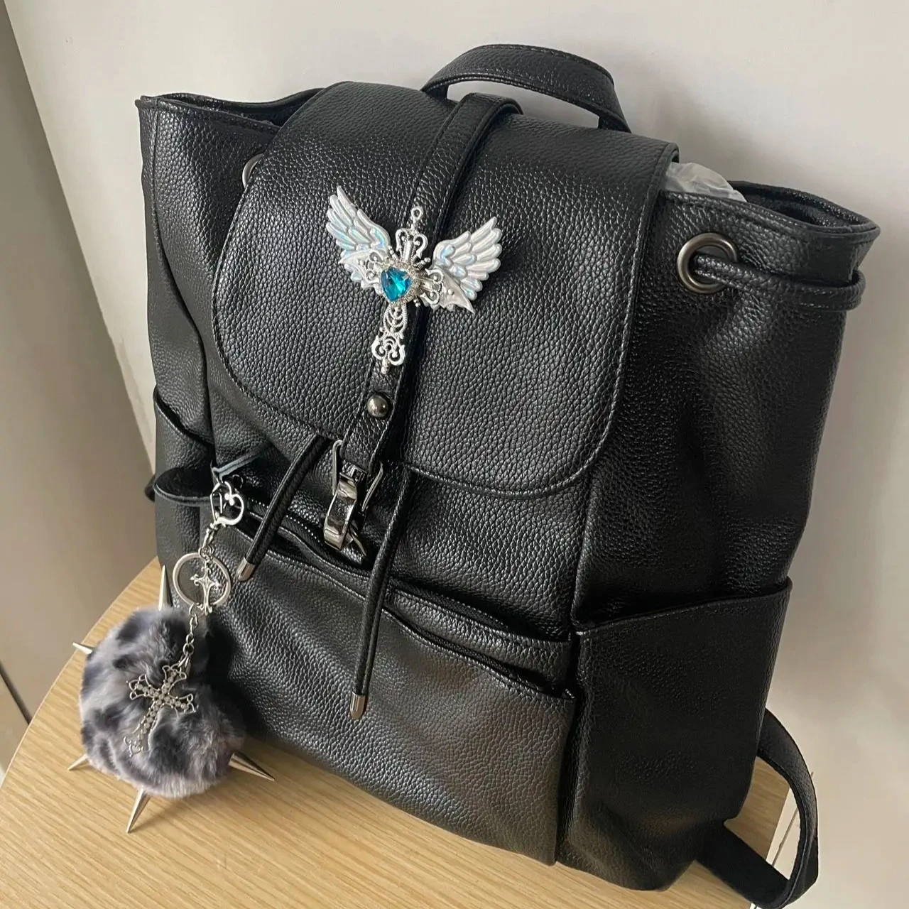 

Women's Drawstring Backpack Fashion Black Leather Backpack with Winged Brooch Edgy Fur Keychain Backpacks