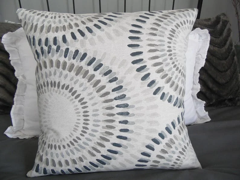 Funda de cojín decorativa neutral con diseño geométrico circular y cuadrado en varios tonos: beige, azul, taupe, caqui y gris.