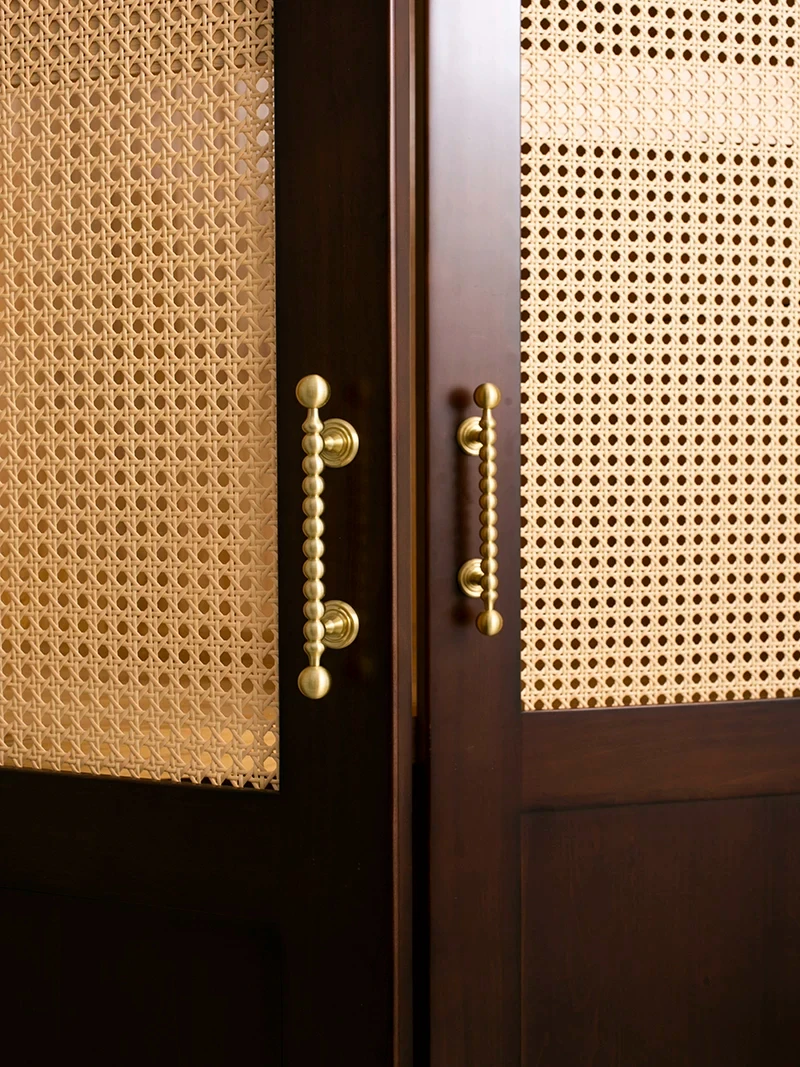Pair of beaded brass cupboard pulls on a woven panel cabinet