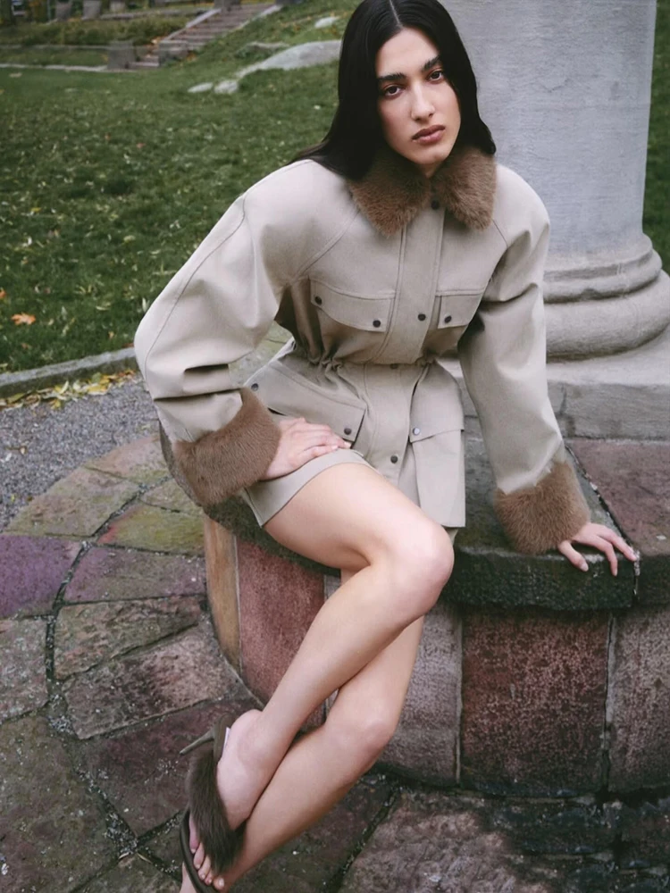 Damska kurtka średniej długości z futrzanym kołnierzem, wieloma kieszeniami i podkreśloną talią, w stylu odzieży roboczej.