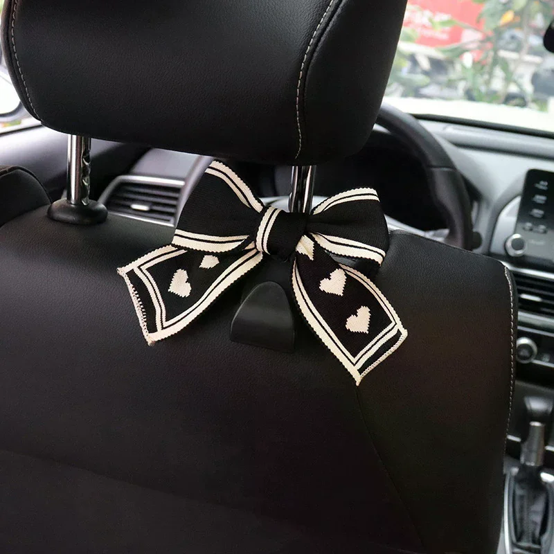Two Car Seat Headrest Hooks With A Black And White Heart-shaped Bow Design; Universal Design Suitable For All Vehicles.