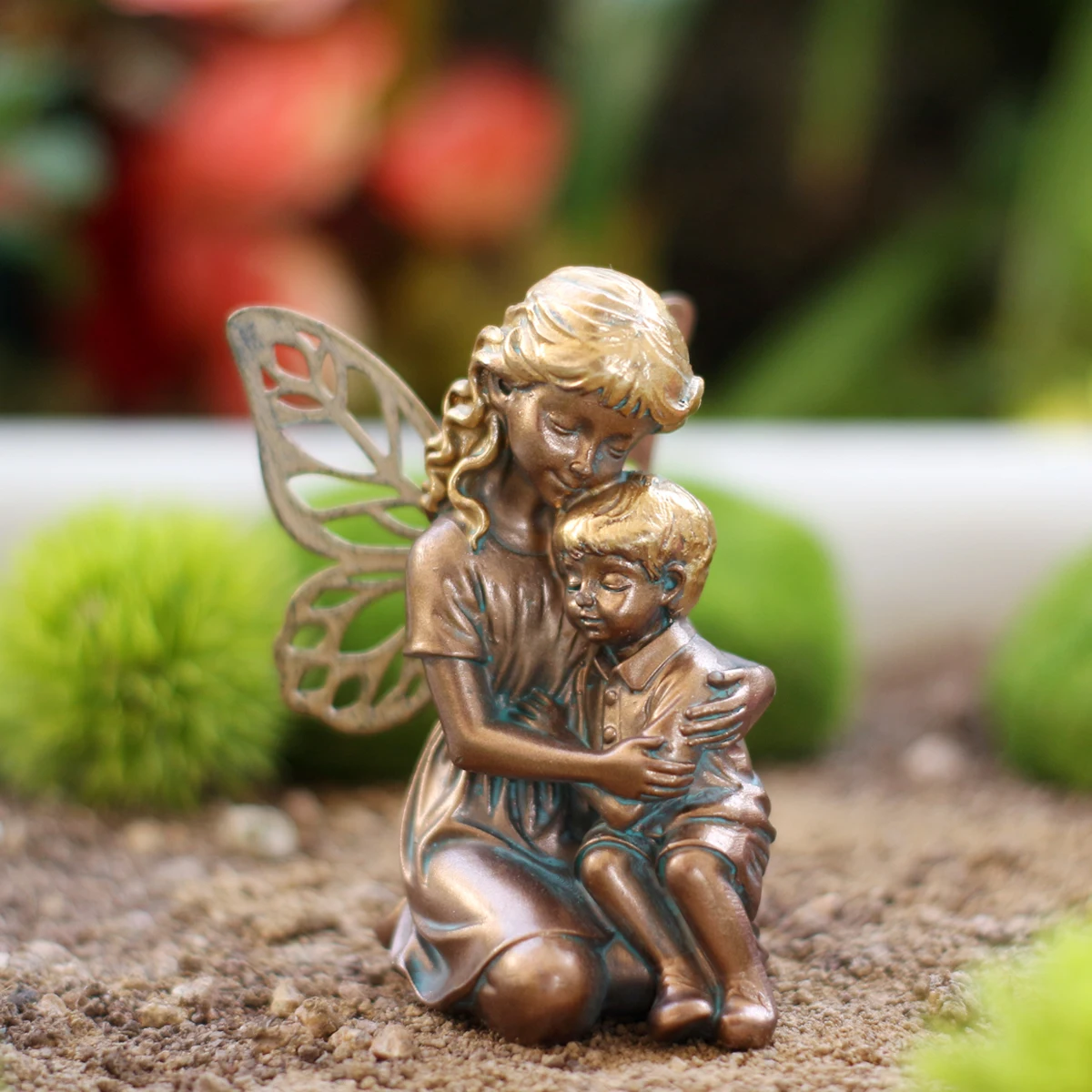 A delicate copper-colored statue of a mother and child in the form of a fairy is placed outdoors. It is suitable for decorating