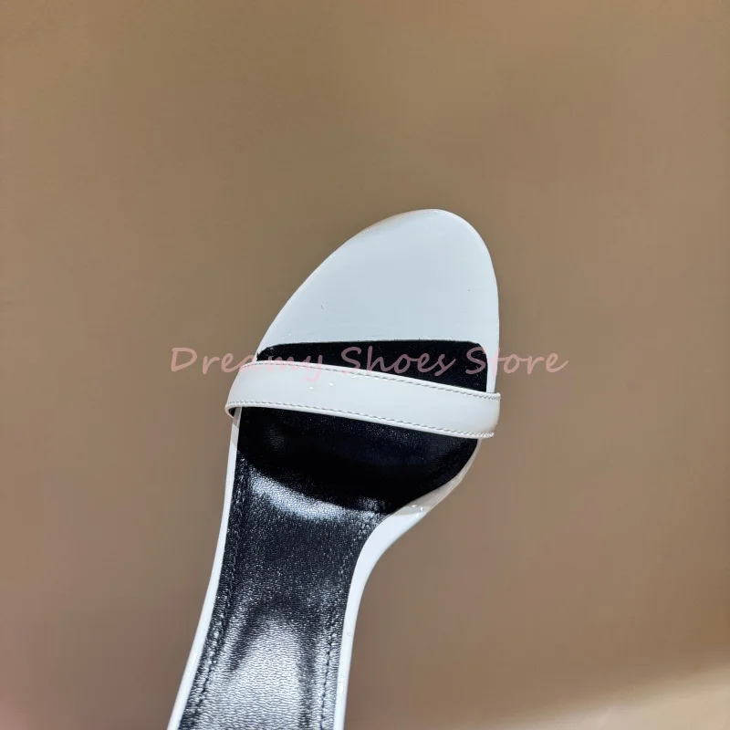 Sandalias de tacón de aguja con una correa en forma de espada blanca para mujer, zapatos de fiesta de charol a la moda con punta abierta y decoración de Metal plateado