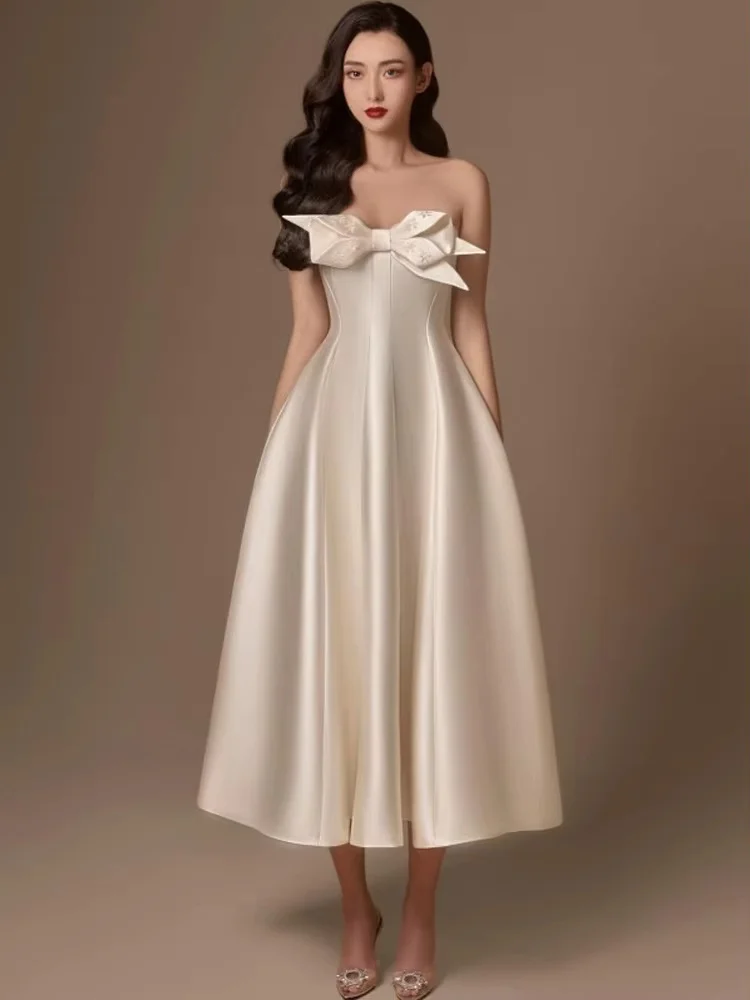 Strapless midi gown decorated with three-dimensional big bow. Loose flared skirt looks light and elegant, plain white brings cla