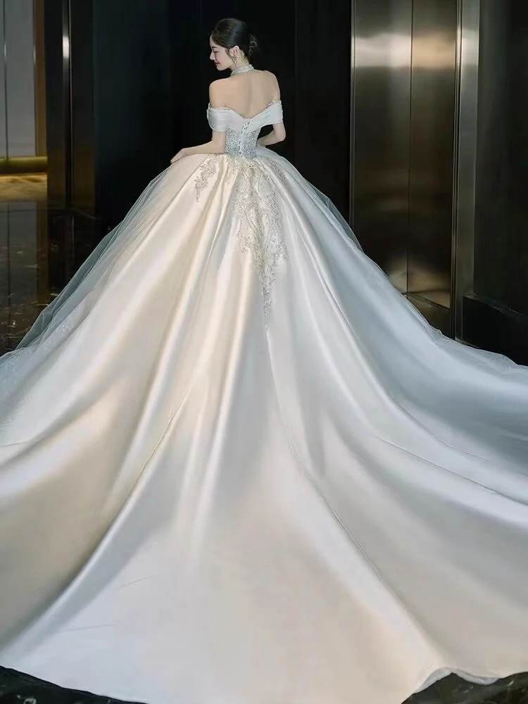 ชุดแต่งงานผ้าซาตินแบบไหล่เดียว ประดับตกแต่งอย่างหรูหรา พร้อมชายกระโปรงยาวแบบสเวปเทรน  ลายมัดย้อมแบบราชวงศ์  ประดับเพชรอะคริลิก  งานปักลายกลางตัวชุด