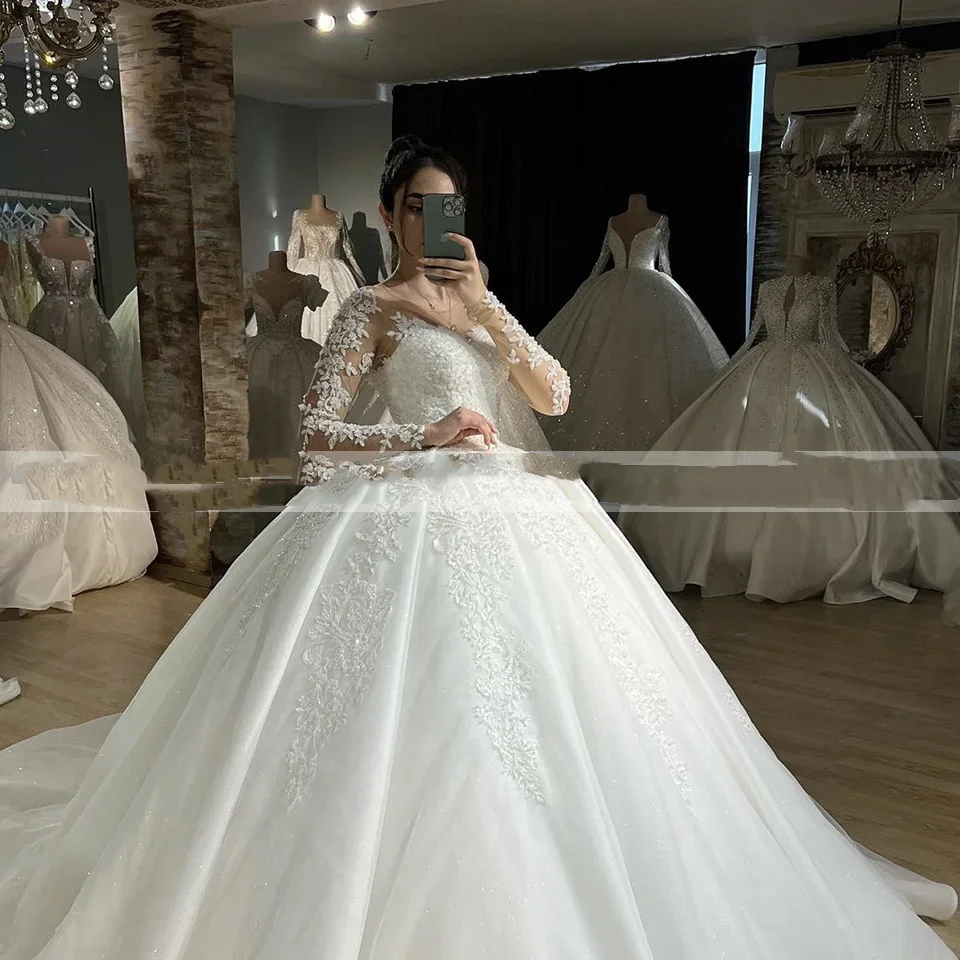 ชุดแต่งงานแบบบอลกาวน์สีขาวสั่งตัดพิเศษ คอทรงโอ แขนยาวเงางาม ประดับลูกไม้  กระโปรงยาวลากพื้น  ผูกเชือกด้านหลัง