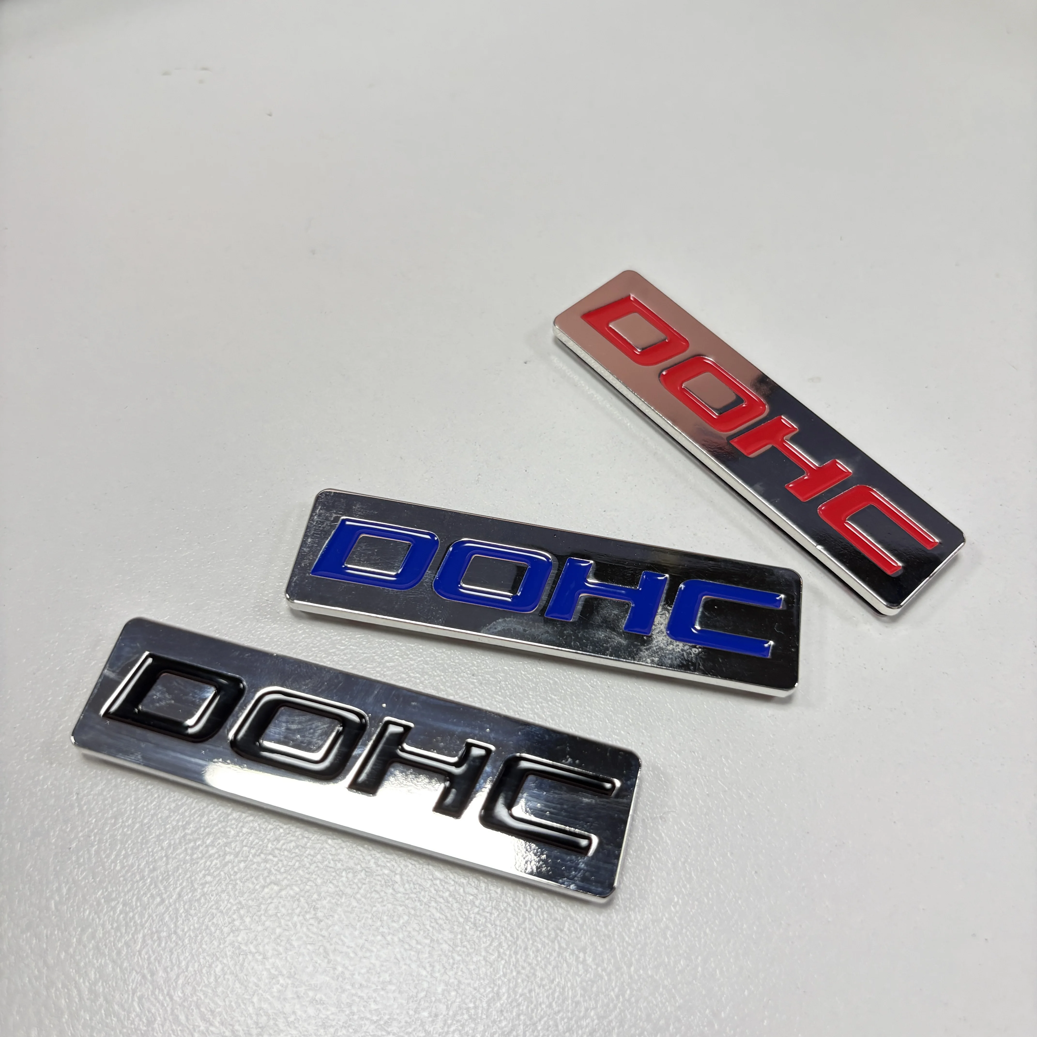 EMBLEMAT METALOWY DOHC MOTYR KORZYSTNYCH ZAWODÓW, NIEBIESKI / CZERWONY / CZARNY, NA BAGAŻNIK, MASKĘ, DRZWI, CHROMOWANY