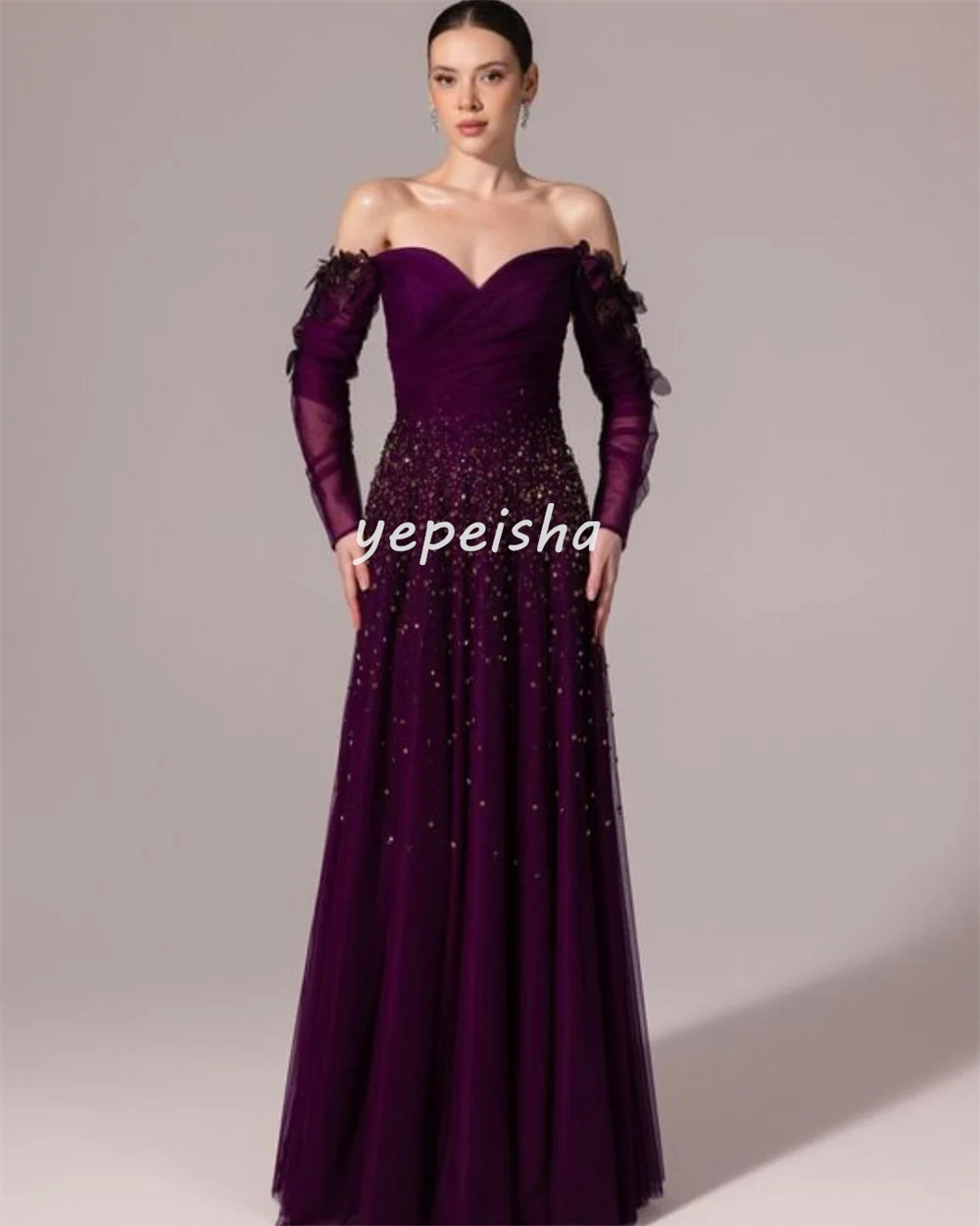 ชุดราตรีทรงเอไลน์แบบเปิดไหล่ ประดับด้วยผ้าทูลล์ระยิบระยับ แต่งดอกไม้ ลูกปัด และเลื่อม ดีไซน์หรูหรา