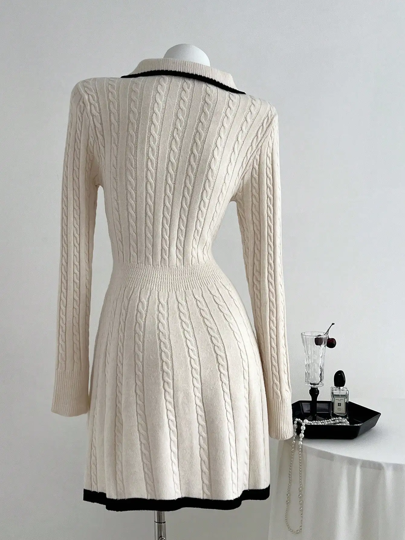 Damska kremowa sukienka swetrowa z długim rękawem, z kołnierzykiem polo, dzianiną w warkocze i czarnymi wykończeniami.