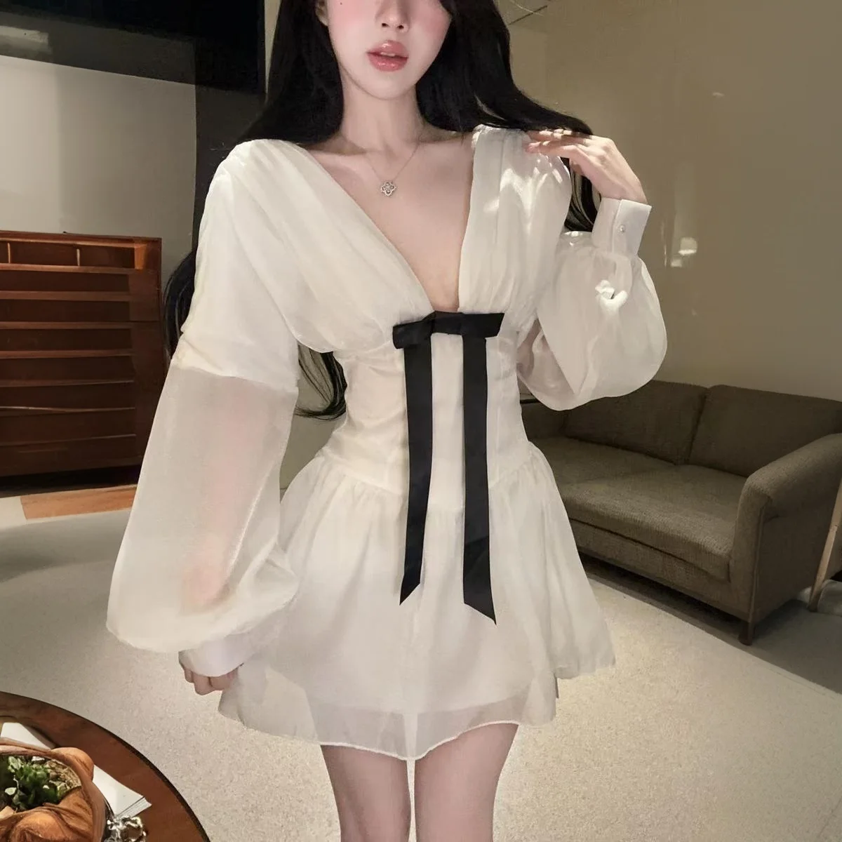 เดรสสั้นสีขาวแบบเซ็กซี่สไตล์ฝรั่งเศส คอวีลึก แต่งโบว์ แขนยาวทรงโคมไฟ ผ้าบาง โชว์เอวเข้ารูป ทรงเอไลน์ เหมาะสำหรับงานวันเกิด